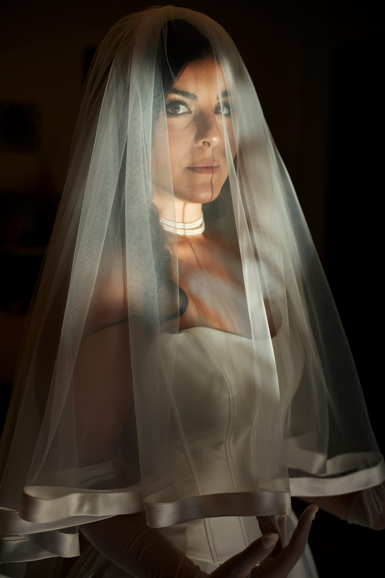 Ritratto di una sposa sotto il velo, illuminata da una luce laterale su fondo scuro