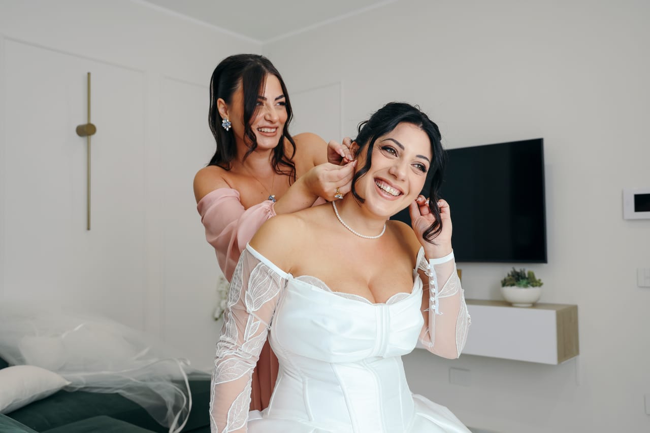 Una donna aiuta la sposa sorridente a indossare gli orecchini